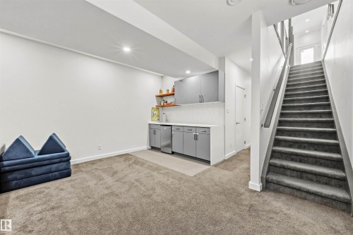 The property features a carpeted room with a built-in wet bar, complete with gray cabinetry, a white countertop, and a stainless steel sink - 10607 127 Street, Edmonton, AB - Indoor