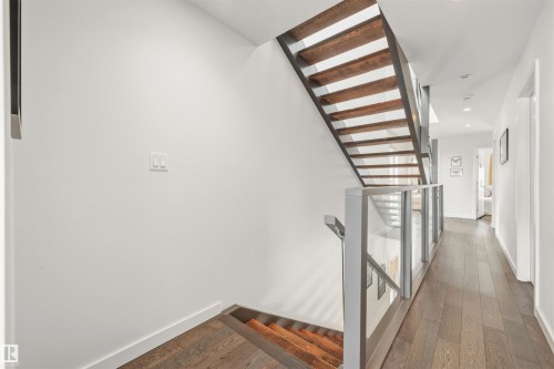 The property features a contemporary staircase with exposed wooden treads and a glass and metal railing, alongside hardwood flooring in the hallway - 10607 127 Street, Edmonton, AB - Indoor Photo Showing Other Room