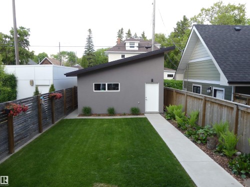 The property includes a spacious lawn area, a paved walkway, and a modern grey outbuilding with white windows and a white door - 10607 127 Street, Edmonton, AB - Outdoor