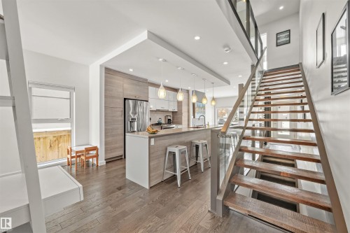 The property features an open-concept layout with hardwood floors throughout, a modern kitchen with a large island, and a distinctive staircase with glass railing - 10607 127 Street, Edmonton, AB - Indoor