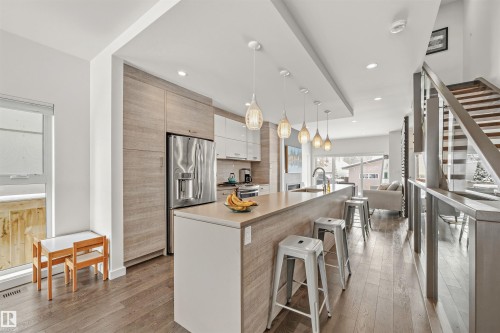 The kitchen features hardwood floors, a large island with seating, pendant lighting, and a stainless steel refrigerator - 10607 127 Street, Edmonton, AB - Indoor Photo Showing Kitchen With Upgraded Kitchen