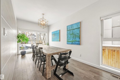 Dining area featuring hardwood floors, a modern chandelier, and large windows providing natural light - 10607 127 Street, Edmonton, AB - Indoor Photo Showing Dining Room