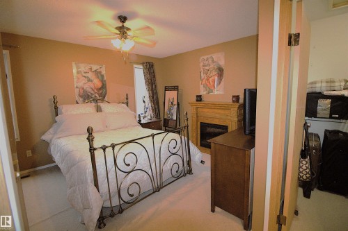 This room features a ceiling fan with integrated lighting, a window with curtains, and a fireplace with a wood-toned mantel - 9347 175 Avenue, Edmonton, AB - Indoor Photo Showing Bedroom