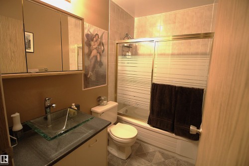 The bathroom features a glass vessel sink set on a dark countertop, a toilet, and a bathtub with a sliding glass shower door - 9347 175 Avenue, Edmonton, AB - Indoor Photo Showing Bathroom