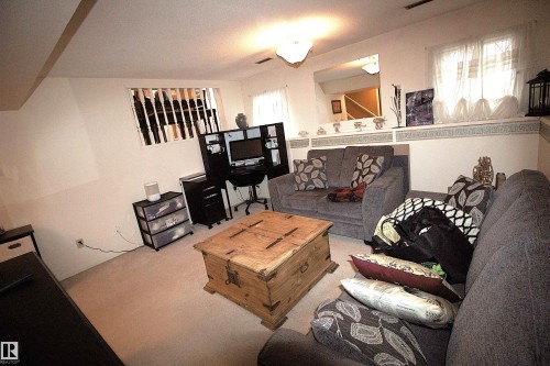This living area features light-colored carpeting, a partial wall with decorative trim, and a window with white curtains - 9347 175 Avenue, Edmonton, AB - Indoor Photo Showing Living Room