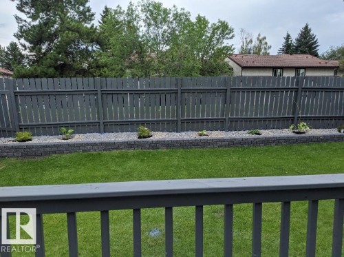 The property features a well-maintained lawn, a dark-painted wooden fence, and a decorative stone retaining wall with plantings - 9347 175 Avenue, Edmonton, AB - Outdoor