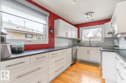 The kitchen features abundant white cabinetry, dark countertops, a white subway tile backsplash, stainless steel appliances, and wood flooring - 10504 60 Street, Edmonton, AB - Indoor Photo Showing Kitchen