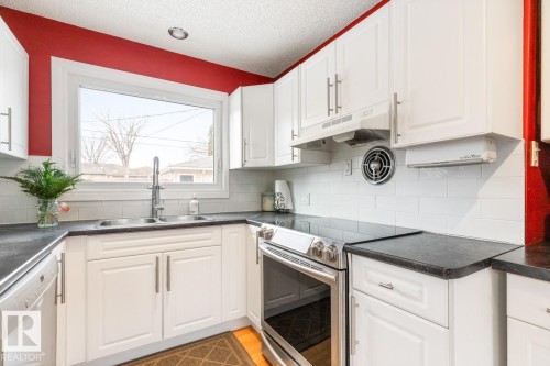 The kitchen features white cabinetry, dark countertops, a stainless steel range, and a white subway tile backsplash - 10504 60 Street, Edmonton, AB - Indoor Photo Showing Kitchen With Double Sink