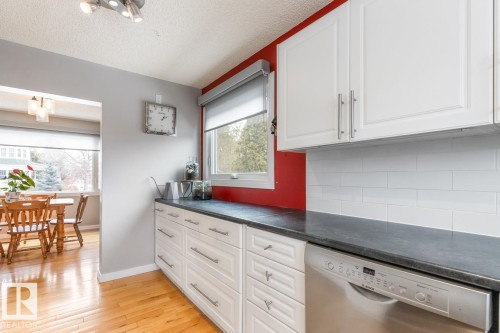 The kitchen features white cabinetry with silver hardware, a stainless steel dishwasher, and a dark countertop - 10504 60 Street, Edmonton, AB - Indoor Photo Showing Kitchen