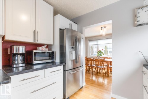 The kitchen features white cabinetry, a stainless steel refrigerator, and dark countertops - 10504 60 Street, Edmonton, AB - Indoor Photo Showing Kitchen