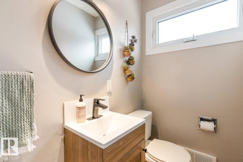 Bathroom featuring a vanity with a white countertop and a modern faucet, a circular mirror, and a window providing natural light - 10504 60 Street, Edmonton, AB - Indoor Photo Showing Bathroom