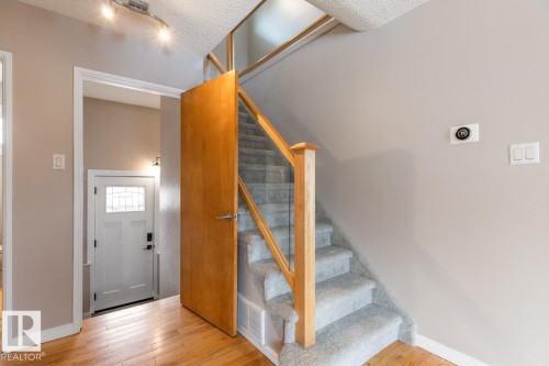 The property features a staircase with light-colored carpeting, a wooden handrail, and glass panels - 10504 60 Street, Edmonton, AB - Indoor Photo Showing Other Room