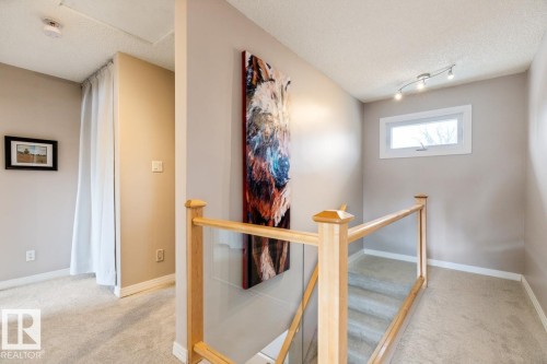 The property features light-colored walls and carpeting, a wooden and glass railing, and a window providing natural light - 10504 60 Street, Edmonton, AB - Indoor Photo Showing Other Room