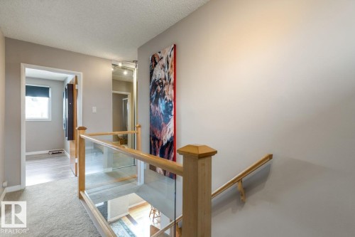 The property features a staircase with a wooden handrail and glass panels, and a hallway with light-colored walls and carpeted flooring - 10504 60 Street, Edmonton, AB - Indoor Photo Showing Other Room