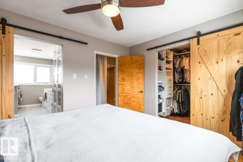 This room features a ceiling fan, light gray walls, and two wooden barn doors on tracks - 10504 60 Street, Edmonton, AB - Indoor Photo Showing Bedroom
