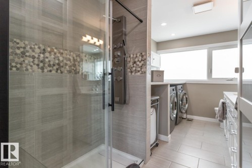 The bathroom features a glass-enclosed shower with tiled walls and a decorative pebble-style accent band - 10504 60 Street, Edmonton, AB - Indoor Photo Showing Laundry Room