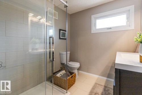 A bathroom featuring a glass-enclosed shower with tiled walls, a toilet, and a vanity with a white countertop and rectangular sink - 10504 60 Street, Edmonton, AB - Indoor Photo Showing Bathroom