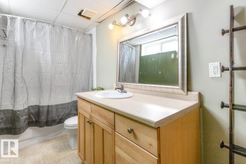 Bathroom featuring a light wood vanity with a light-colored countertop and an integrated sink, a framed mirror, and a shower with a white bathtub - 10504 60 Street, Edmonton, AB - Indoor Photo Showing Bathroom