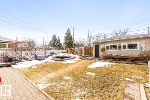 The property features a spacious rear yard with a paved patio area and a separate building with a dark entry door and white-framed windows - 10504 60 Street, Edmonton, AB - Outdoor