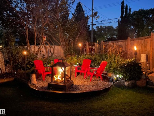 The property features a well-lit outdoor area with a fire pit, surrounded by gravel and four red Adirondack chairs - 10504 60 Street, Edmonton, AB - Outdoor