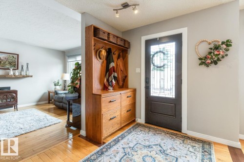 Foyer with hardwood flooring, a dark entry door with decorative glass inserts, and an integrated wooden storage unit featuring hooks and drawers - 10504 60 Street, Edmonton, AB - Indoor Photo Showing Other Room