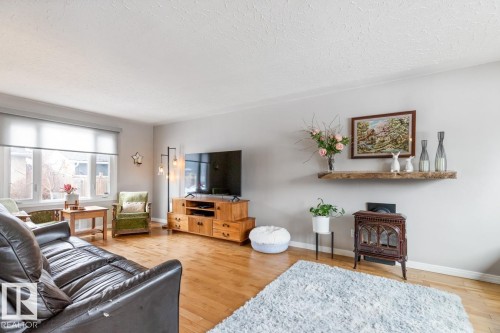 Living area featuring hardwood flooring, a large window providing natural light, and a wall-mounted wooden shelf - 10504 60 Street, Edmonton, AB - Indoor Photo Showing Living Room