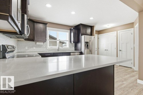 Contemporary kitchen featuring dark wood cabinetry, a light-colored island countertop, stainless steel appliances, and a tiled backsplash - 2 Wingate Way, Fort Saskatchewan, AB - Indoor Photo Showing Kitchen