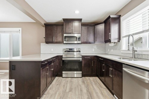 The kitchen features dark wood cabinetry, stainless steel appliances, light countertops, and a subway tile backsplash - 2 Wingate Way, Fort Saskatchewan, AB - Indoor Photo Showing Kitchen With Double Sink With Upgraded Kitchen
