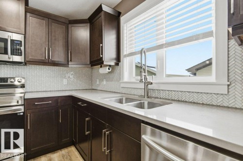 The kitchen features dark wood cabinetry, light-colored countertops, a double basin sink with a gooseneck faucet, and a patterned tile backsplash - 2 Wingate Way, Fort Saskatchewan, AB - Indoor Photo Showing Kitchen With Double Sink With Upgraded Kitchen