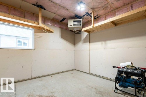 This space features a concrete floor, exposed ceiling joists with insulation, a window providing natural light, and a wall-mounted heater - 2 Wingate Way, Fort Saskatchewan, AB - Indoor