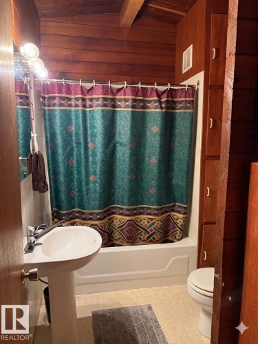 Bathroom featuring wood-paneled walls and ceiling, a white pedestal sink with chrome faucet, a white bathtub, and built-in wood cabinetry - 1040 &1040 A&B Mitchell Beach Beach, Rural Leduc County, AB 