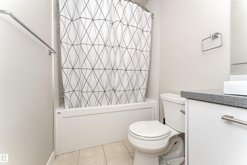 The bathroom features a bathtub with a shower, a toilet, and a vanity with a rectangular sink and dark countertop - 313 10418 81 Avenue, Edmonton, AB - Indoor Photo Showing Bathroom