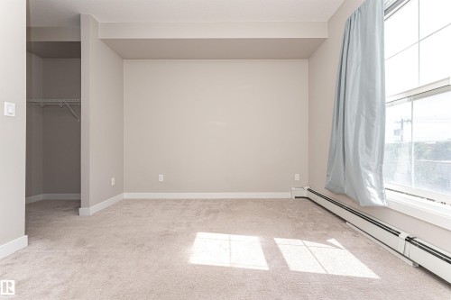 This room features light-colored carpeting, a window with a light blue curtain, and a baseboard heater - 313 10418 81 Avenue, Edmonton, AB - Indoor Photo Showing Other Room