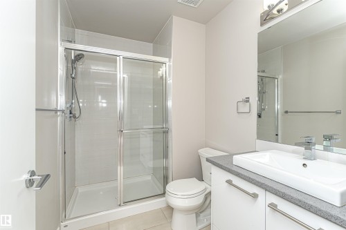 The bathroom features a glass-enclosed shower with a tiled surround, a vanity with a white countertop and rectangular sink, and a mirror with overhead lighting - 313 10418 81 Avenue, Edmonton, AB - Indoor Photo Showing Bathroom