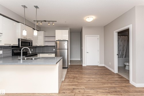 Open concept kitchen featuring an island with a sink, white cabinetry, stainless steel appliances, and track lighting - 313 10418 81 Avenue, Edmonton, AB - Indoor Photo Showing Kitchen With Double Sink
