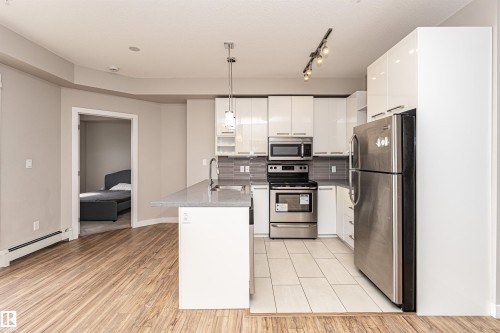 The property features a kitchen with white cabinetry, stainless steel appliances, and a grey tiled backsplash - 313 10418 81 Avenue, Edmonton, AB - Indoor Photo Showing Kitchen