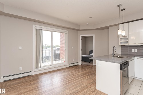 Open concept living area with wood plank flooring, a sliding glass door leading to a balcony, and a modern kitchen featuring an island with a sink and pendant lighting - 313 10418 81 Avenue, Edmonton, AB - Indoor Photo Showing Kitchen