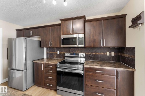 The kitchen features dark wood cabinetry, stainless steel appliances, and contrasting countertops - 84 Calvert Wynd, Fort Saskatchewan, AB - Indoor Photo Showing Kitchen
