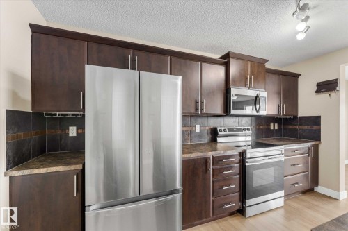 The kitchen features dark wood cabinetry, stainless steel appliances, a dark tile backsplash, and light-colored flooring - 84 Calvert Wynd, Fort Saskatchewan, AB - Indoor Photo Showing Kitchen