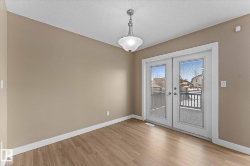This room features light wood-style flooring, a ceiling-mounted light fixture, and double glass-paneled doors with white trim that open to an exterior area - 84 Calvert Wynd, Fort Saskatchewan, AB - Indoor Photo Showing Other Room