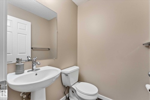 The bathroom features a pedestal sink with a chrome faucet, a toilet, and a mirror - 84 Calvert Wynd, Fort Saskatchewan, AB - Indoor Photo Showing Bathroom