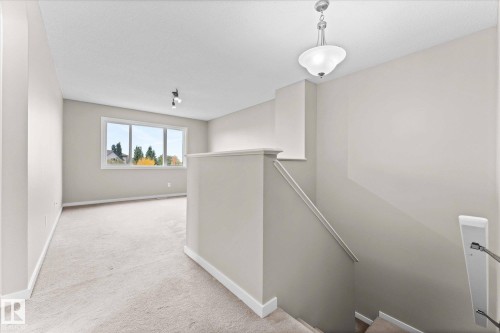 This carpeted area features neutral-toned walls, a window providing natural light and exterior views, and a light fixture on the ceiling - 84 Calvert Wynd, Fort Saskatchewan, AB - Indoor Photo Showing Other Room