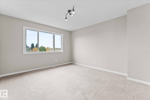 This room features light-colored carpeting, neutral painted walls, and a large window with a white frame - 84 Calvert Wynd, Fort Saskatchewan, AB - Indoor Photo Showing Other Room