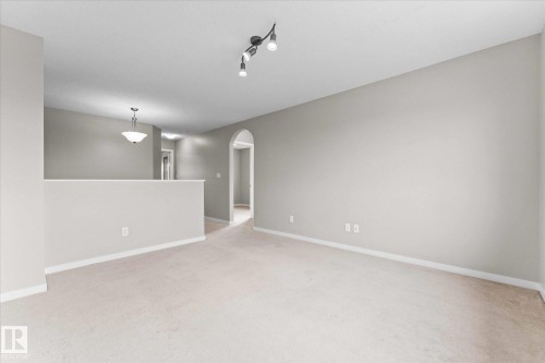 Inviting living area featuring light-colored carpeting, a track lighting fixture, and an arched doorway - 84 Calvert Wynd, Fort Saskatchewan, AB - Indoor Photo Showing Other Room