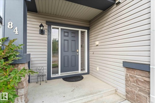 The property features a front entrance with a dark gray door and a storm door, set within light gray siding - 84 Calvert Wynd, Fort Saskatchewan, AB - Outdoor With Exterior