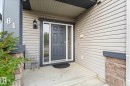 The property features a front entrance with a dark gray door and a storm door, set within light gray siding - 84 Calvert Wynd, Fort Saskatchewan, AB  - Outdoor With Exterior 