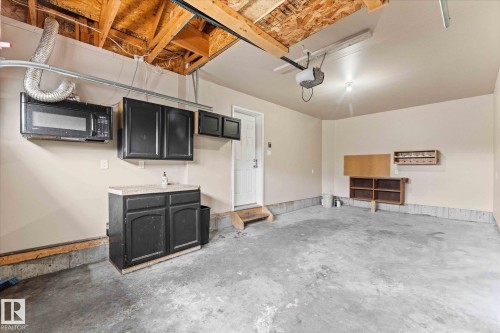 The garage features a concrete floor, built-in cabinetry with a countertop, and a wall-mounted microwave - 84 Calvert Wynd, Fort Saskatchewan, AB - Indoor