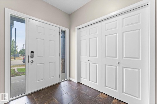 Entryway featuring a white paneled door with sidelight windows, dark tile flooring, and white bifold closet doors - 84 Calvert Wynd, Fort Saskatchewan, AB - Indoor Photo Showing Other Room