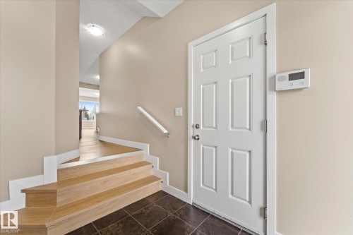Inviting entryway featuring a white paneled door, a light wood staircase, dark floor tiling, and a white handrail - 84 Calvert Wynd, Fort Saskatchewan, AB - Indoor Photo Showing Other Room