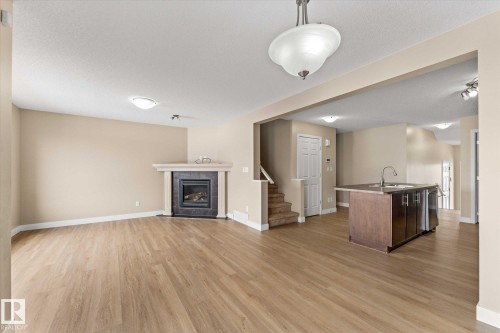 Living area featuring light-toned flooring, a fireplace with a stone surround, and an open concept view of the kitchen island - 84 Calvert Wynd, Fort Saskatchewan, AB - Indoor With Fireplace